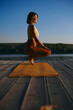 © chika_milan - The tranquil woman is practicing yoga on the dock while crouching and balancing. She is in the Squatting Toe Balance yoga pose.