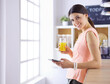 © lenets_tan - Smiling pretty woman looking at mobile phone and holding glass of orange juice while having breakfast in a kitchen.