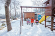 girl help swinging her brother and sister during playing in snowy playground