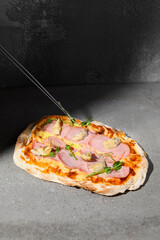 Sticker - Cooked Italian pizza with ham and artichokes on dark background. Pinsa with ham on gray stone table with hard shadow. Roman pizza with ham and artichokes on concrete background. Pinsa from chef.