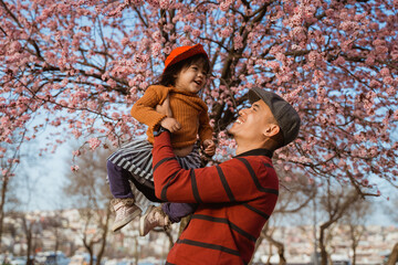 happy father and daughter looking at cherry blossom in the park