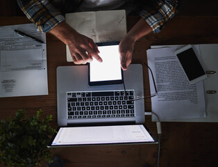 Fototapete - Laptop and tablet in the hands of a man working late at night in the office from above. Deadline and overtime at a desk with technology and paper work. Sending an email reading or typing a report