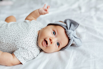 candid lifestyle portrait of cute caucasian blonde baby two months old lying on white bed at home