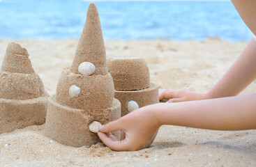 Canvas Print - Child decorating sand castle with shell on beach, closeup