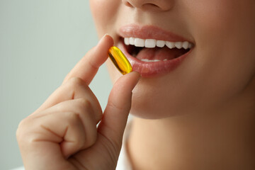 Wall Mural - Young woman taking dietary supplement pill on blurred background, closeup