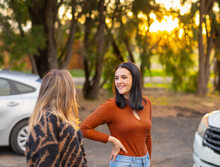 Two Teenagers Outside Near Vehicles With Trees In Background