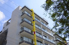 Pipe For Debris, Waste Tube. Suspended Sections Of Yellow Garbage Chute On A Facade Of Building Under Construction Against Blue Sky.  Plastic Garbage Chute Fixed On Facade. Repair In Apartment