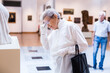 © caftor - mature woman examines sculpture in an exhibition in hall of an art museum