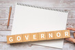 知事・長官・理事のイメージ｜「GOVERNOR」と書かれたブロック、ノート、ペン、手
