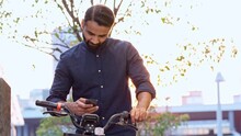 Indian business man holding smartphone using bike rental digital phone app scanning qr code to rent electric bicycle in city public eco transport mobile application standing on urban park on sunset.