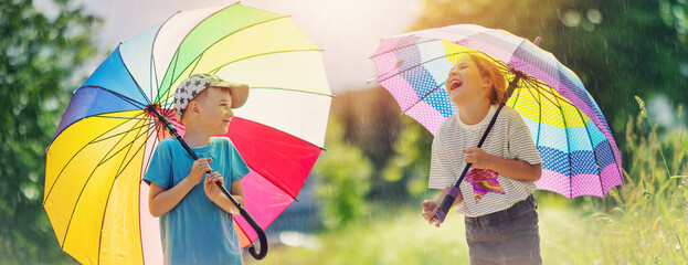 Wall Mural - Happy children standing under the rain with colourful umbrellas in their hands.