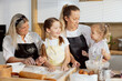 © ABCreative - Preschooler daughter wearing apronh holding spoon in arm telling own recipe of kneading dough for cooking baking cookies homemade pizza. Elderly granny mom and older sister listening smiling.