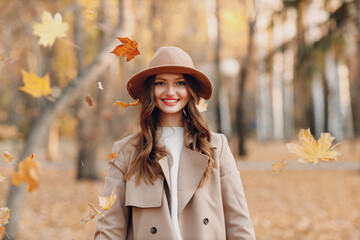 Beautiful smiling girl at autumn park flying fall yellow foliage leaves.