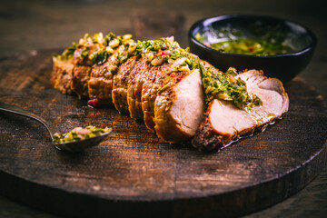 Homemade grilled pork steak with chimichurri verde sauce on cutting board on dark background