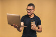 © denis_vermenko - Young smiling african american black man standing and using laptop computer isolated over beige background. Drinking coffee.