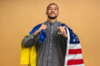 © denis_vermenko - Portrait of positive african american black guy holding usa and ukrainian flags, isolated over beige background.