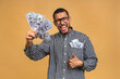 © denis_vermenko - Happy winner! Young rich african american man in casual t-shirt holding money dollar bills with surprise isolated over beige wall.