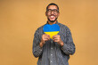 © denis_vermenko - Portrait of positive african american black guy holding ukrainian flag, isolated over beige background.