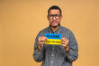 © denis_vermenko - Stop war! Save Ukraine! Portrait of sad negative african american black guy holding ukrainian flag, isolated over beige background.