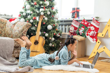 Christmas tree in a large living room. Little girl plays near the Christmas tree. A girl with a laptop communicates with friends.