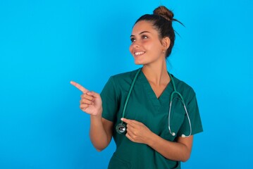 beautiful doctor woman wearing medical uniform over blue background smile excited directing fingers look empty space