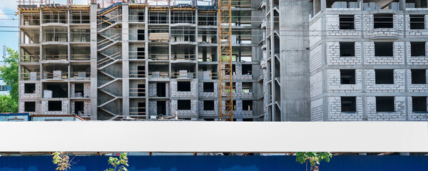 Wall Mural - Long white advertising billboard mounted at city street against unfinished building front panoramic view