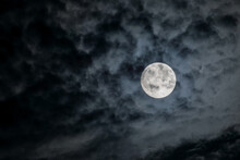 Full Moon At Night. The Illuminated Face Of The Moon Is Wrapped In A Cloud Cover That Covers It In A Veiled Way.