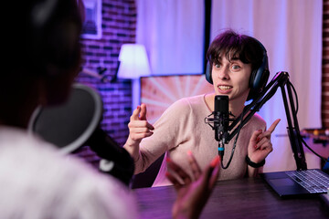 Wall Mural - Female presenter interviewing young woman with podcast equipment, having conversation to broadcast live on channel. Women meeting in studio to record discussion on social media.