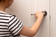 Girl stands near a closed door and holds the door handle. A child is alone at home in a dangerous situation. Girl opens the door to the room