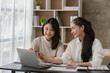 © ArLawKa - Two young Asian female accountants discuss working on investment projects and planning strategies using laptop computers in their office.