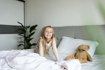 Wall Mural - Candid lifestyle portrait of Cheerful caucasian child eight years old in pajamas having fun on bed at cozy home at morning after awake