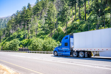 Long haul blue big rig semi truck transporting cargo in dry van semi trailer running on the highway road in Columbia Gorge