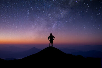 Wall Mural - Silhouette of young man standing alone on top of mountain enjoying watching beautiful of night sky, star and milky way over the sky background. He was happy to travel alone.