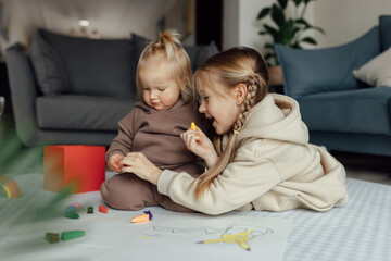 little caucasian siblings drawing together on floor in living room at home. happy girl eight years o