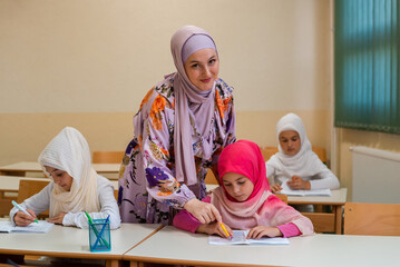 Wall Mural - Female hijab Muslim teacher helps school children to finish the lesson in the classroom.	