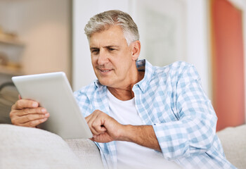 Wall Mural - Mature and senior man browsing on tablet, searching the internet and scrolling on social media while sitting on the couch at home. One retired male reading, checking and replying to messages online