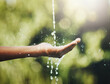 © Nikish Hiraman/peopleimages.com - Hygiene, washing and saving water with hands against a green nature background. Closeup of one person holding out their palm to save, conserve and refresh with water in a park, garden or backyard