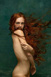 Young attractive redhead girl with long curly hair wearing nude color lingerie isolated over dark green background. Magic look. Concept of beauty, art
