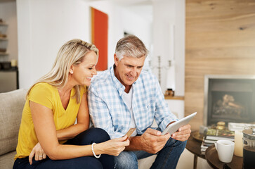 Poster - Beautiful, smiling mature couple buying online, shopping on their digital tablet together on their home living room sofa. Husband making financial payments through internet banking with his wife