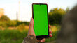 © seeasign - Kharkiv, Ukraine, 01.8.2022, close-up, a soldier in camouflage uniform holds a smartphone with a vertical green screen chroma key smartphone technology
