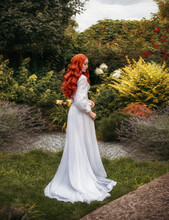 Fantasy Photo Red-haired Woman Walks In Summer Blooming Garden. Long Flowing Red Hair White Vintage Old Historical Style Dress Hem Train. Girl Sexy Aristocrat Back Rear View Leaves. Green Nature Trees