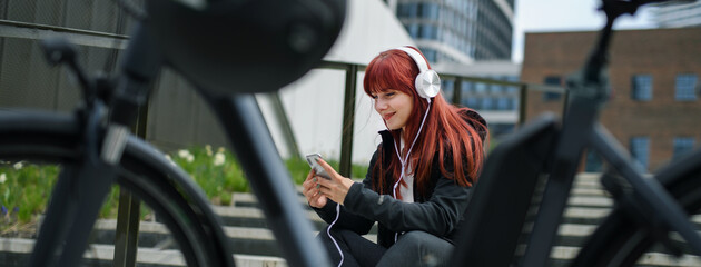 Portrait of businesswoman commuter on the way to work with bike, resting listening to music, sustainable lifestyle concept. Wide shot.