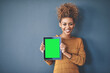 © Camerene P/peopleimages.com - African female holding green screen tablet copyspace. Cute, attractive and smiling young afro woman standing and showing a mobile device.Happy, cheerful and ethnic woman after buying new app.