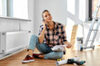 repair, people and real estate concept - woman with papers on clipboard calling on smartphone sitting on floor at home