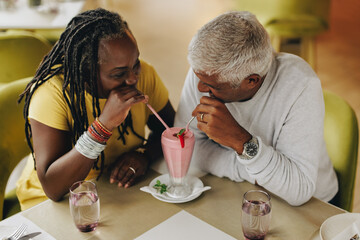 Wall Mural - Mature couple sharing a milkshake in a cafe