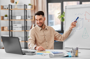 distant education, school and remote job concept - happy smiling male math teacher with laptop compute showing geometric shapes on flip chart having online class or video call at home office