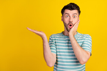 Poster - Photo of ecstatic impressed man dressed striped t-shirt demonstrating empty space hand on cheek isolated on yellow color background