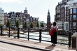 Mujer joven parada en un puente de la ciudad de Ámsterdam. Vistas de edificios tradicionales holandeses