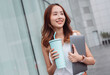 © Kiattisak - Smiling asian businesswoman use smartphone and hold reusable eco-friendly ecological cup and laptop computer while commuting in city in the morning