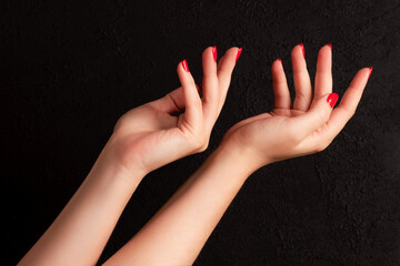 Wall Mural - Female hands with beautiful manicure - red nails on dark black background. Nail, skin care concept